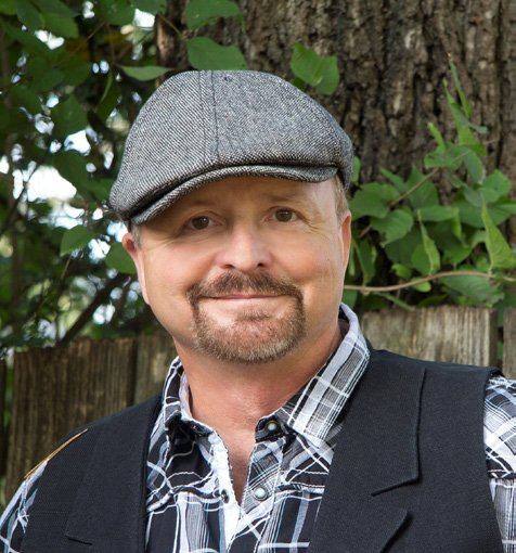Frank Myers in a gray flat cap and plaid shirt, smiling outdoors