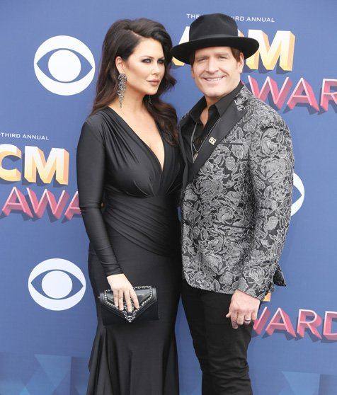 A couple posing on the red carpet in front of an ACM Awards backdrop