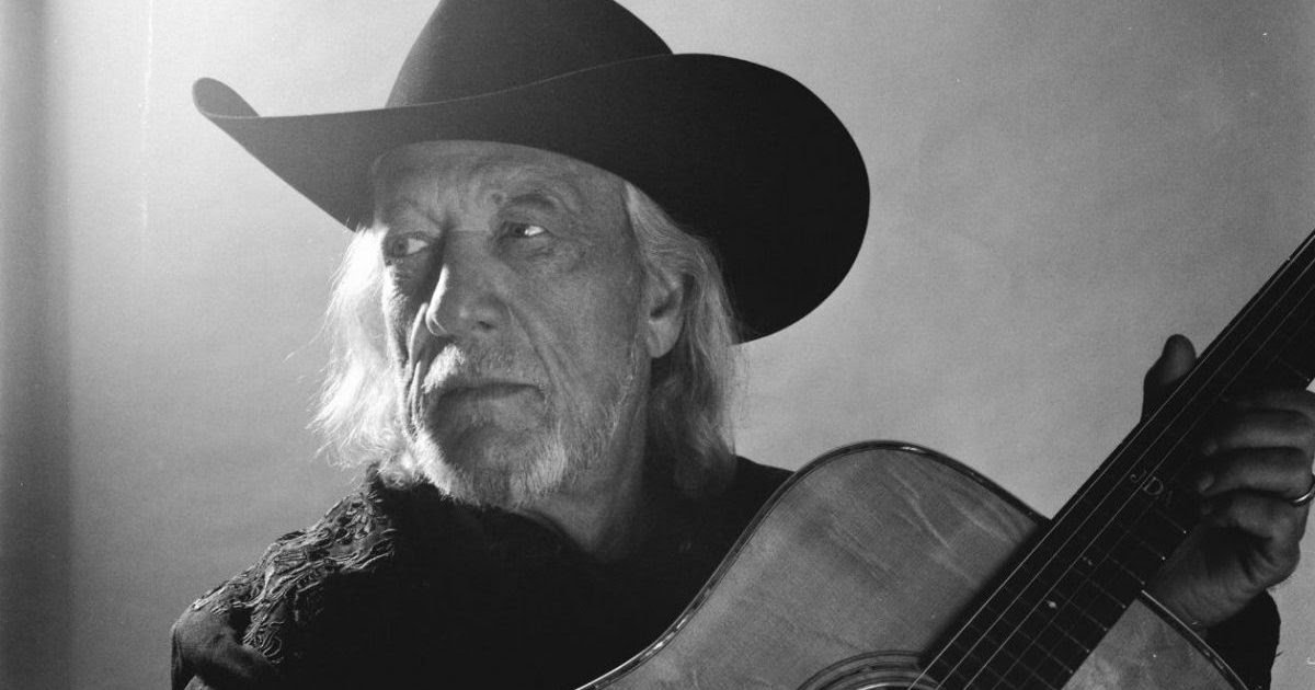 John Anderson in a black cowboy hat, holding an acoustic guitar