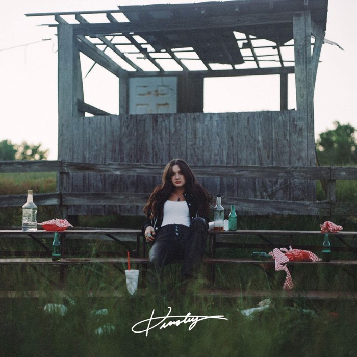 Cover of Kinsley's Learn To Live EP: the singer seated on old bleachers in a field